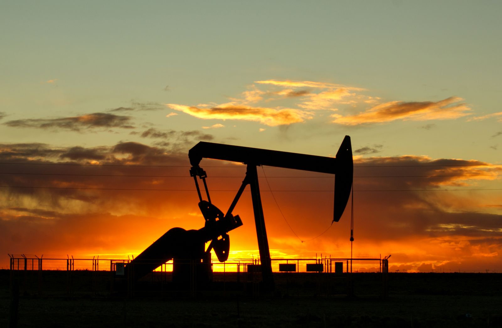 Oil production wellhead silhouetted against a sunset